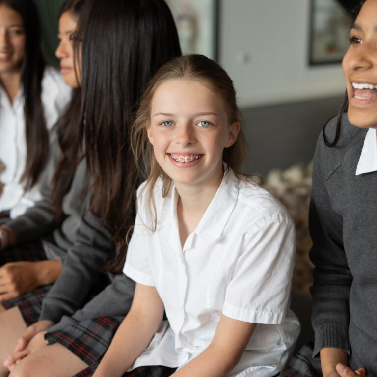 Group of girls in school uniforms sitting together, smiling at the camera (center girl has braces)