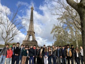 Group of students posing for a photo in front of the Eiffel Tower on a clear day.