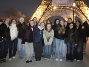 Group of young people posing for a photo at night in front of a lit Eiffel Tower replica behind them.