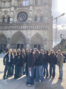 Group of teenagers posing in front of Notre-Dame Cathedral in Paris, with the cathedral's façade and rose window behind them.