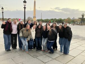 Group of young people posing for a photo in front of Paris landmarks, with the Luxor Obelisk and Eiffel Tower in the background.