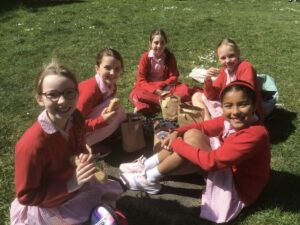 Group of girls in red sweaters and striped dresses having a picnic on the grass.