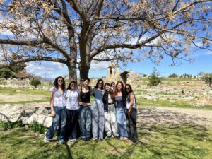 Group of young women posing together outdoors under a blossoming tree with ancient ruins in the background.