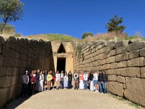 Group of people posing together inside a sunlit ancient stone quarry or ruin with tall stone walls and a clear blue sky above.