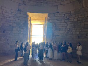 Group of tourists standing along a stone-walled chamber, facing a bright doorway at the far end.