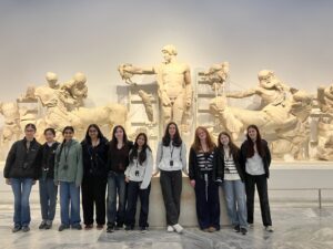 Group of students posing in front of large white classical statues inside a museum.