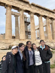 Five students pose together in front of ancient stone temple columns, with scaffolding visible in the background.