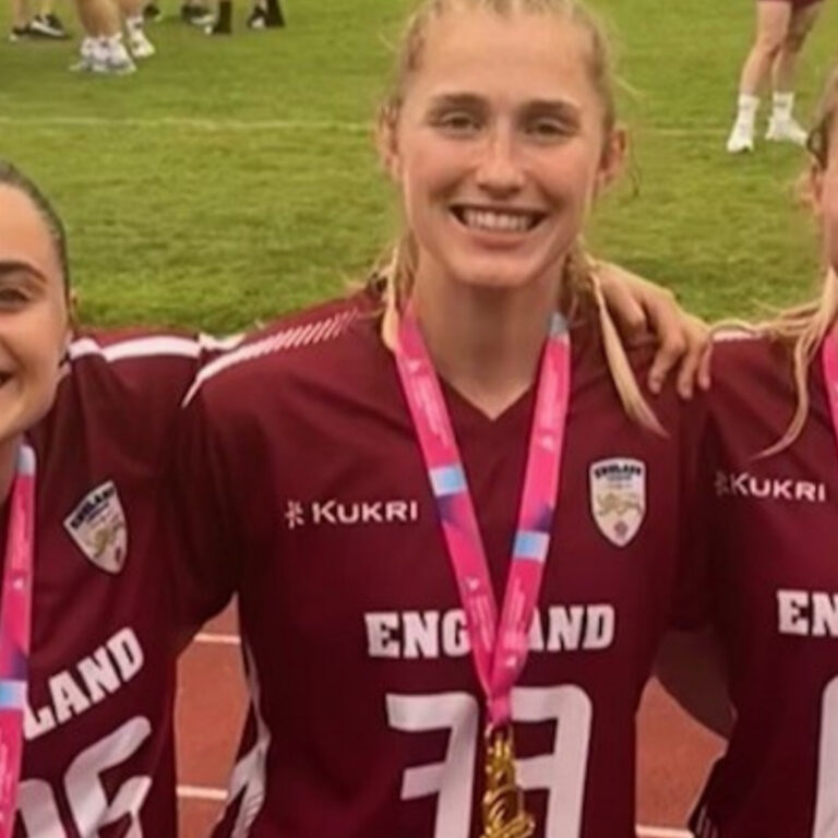 Three female England athletes in maroon jerseys with medals around their necks, smiling on a track field.