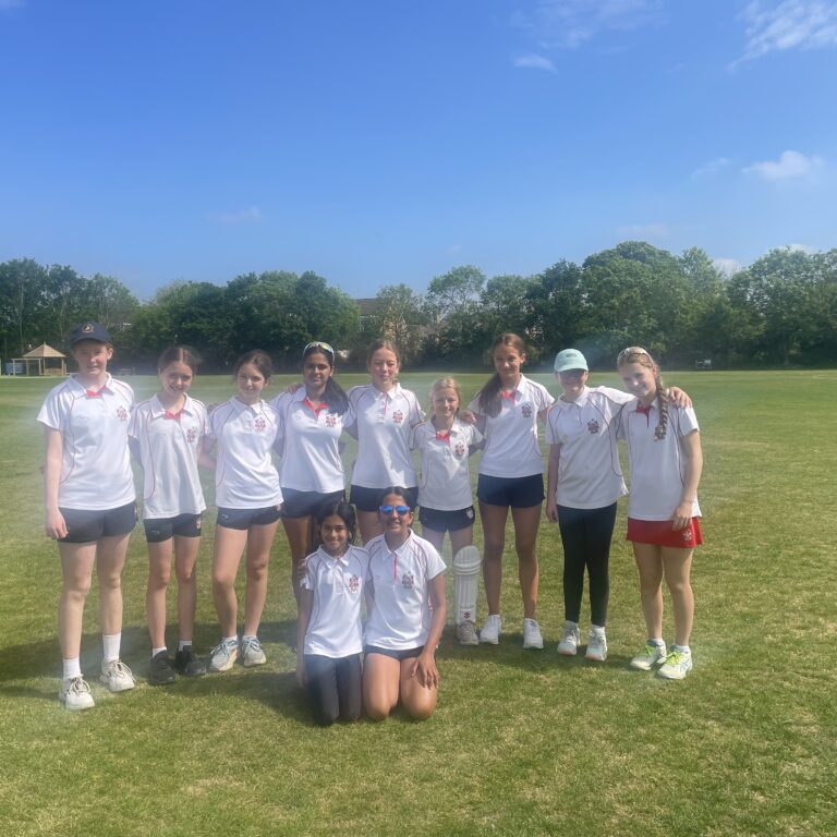 Group of young girls in white polo shirts posing together on a grassy field under a clear blue sky, smiling after a sports practice.