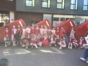 Group of schoolchildren in pink uniforms posing in front of red telephone booth sculptures outside a modern building.