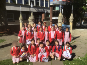 Group of schoolchildren in red cardigans and pink striped dresses posing for a photo outside a building with decorative stone pinnacles.