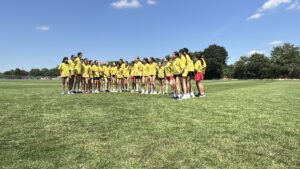 Group of people in yellow shirts lined up on a grassy field under a blue sky, outdoors.