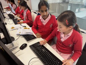 Group of students in red sweaters working on desktop computers in a bright classroom.