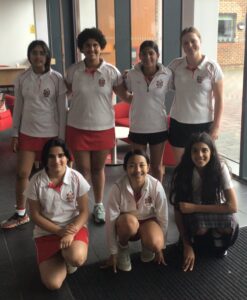 Group of students in white and red school uniforms posing indoors by large windows.