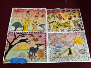 Colorful children's drawings of jungle animals on folded paper panels, featuring a yellow giraffe, cheetah, monkeys, and other creatures, with a blue tissue embellishment on the left side.