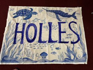 Blue ink illustration on fabric showing an underwater scene with a turtle, fish, coral, bubbles and large geometric shapes that resemble letters or symbols.