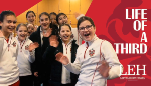 Smiling group of girls in white school uniforms posing and waving in a hallway; a bold red poster area with white text fills the right side.